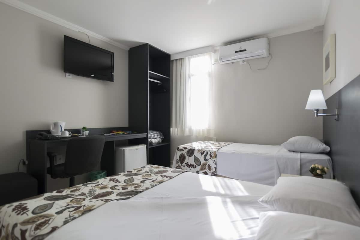 Une chambre d’hôtel avec deux lits, un bureau avec une chaise, une télévision, un appareil de climatisation et une fenêtre avec des rideaux.
