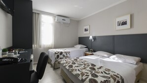 A hotel room with two beds, a desk, a chair, a nightstand, a lamp, and a window with curtains. - Paulista Garden Hotel (São Paulo)