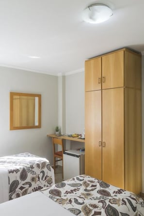 Une chambre avec deux lits, une armoire en bois, un bureau avec une chaise et une petite table avec une plante.