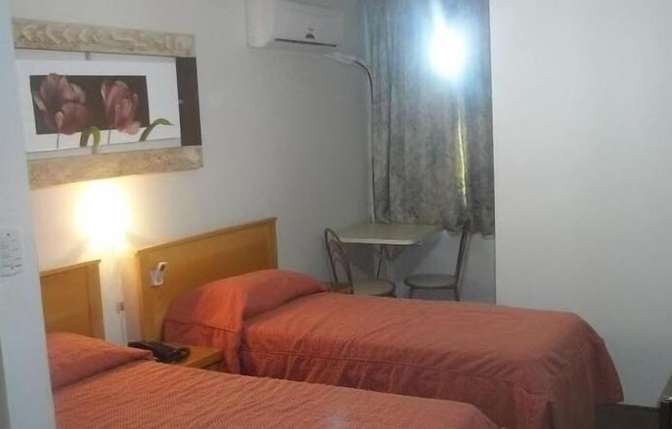 Una habitación con dos camas, una mesita y una silla.