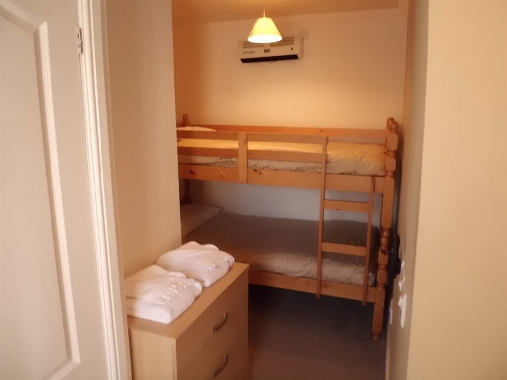 A small, narrow room with two bunk beds, a wooden dresser, and a ceiling fan.