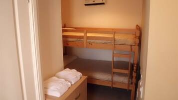 A small, narrow room with two bunk beds, a wooden dresser, and a ceiling fan.