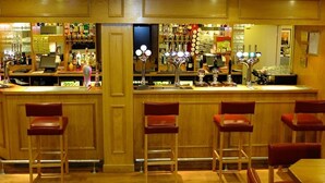 Una zona de bar con paneles de madera, una barra con caja registradora y varios taburetes.