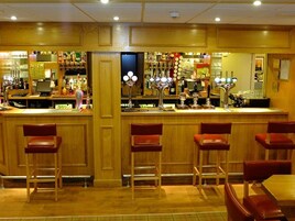 A bar area with wooden paneling, a counter with a cash register, and multiple stools.