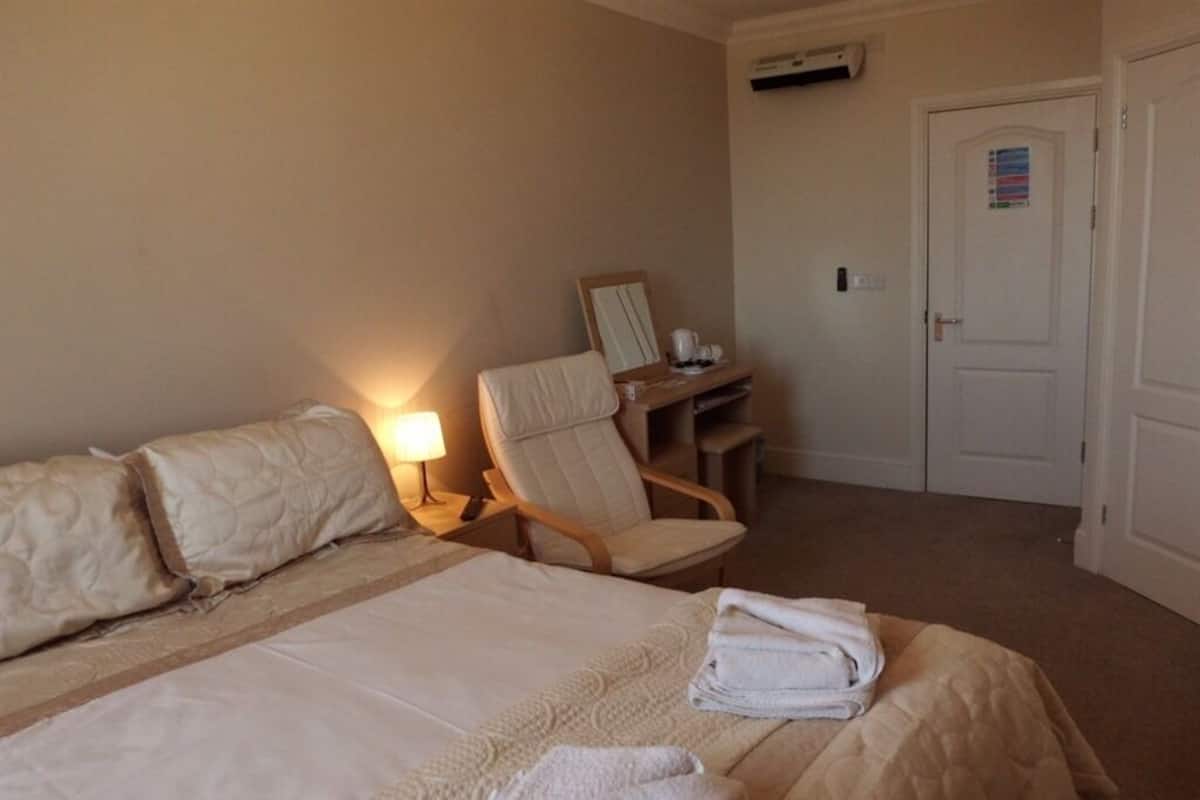 A hotel room with a bed, a chair, a desk, and a door.