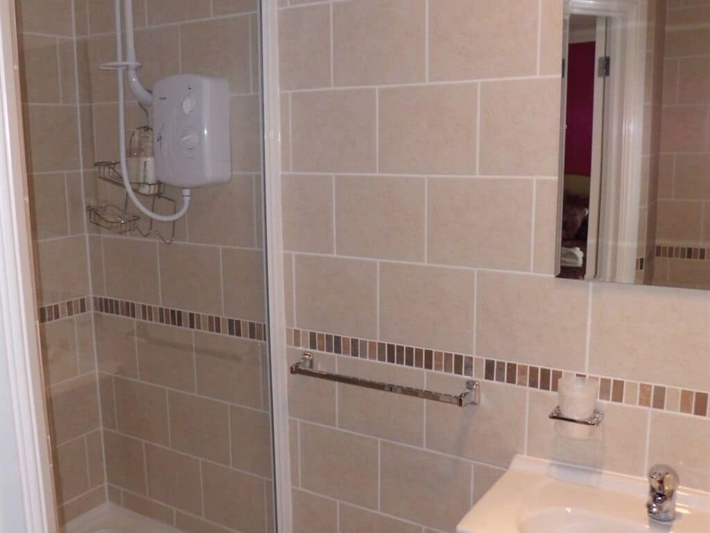 Een badkamer met beige tegels, een douchecabine van glas, een wit wastafelmeubel en een handdoekrek.