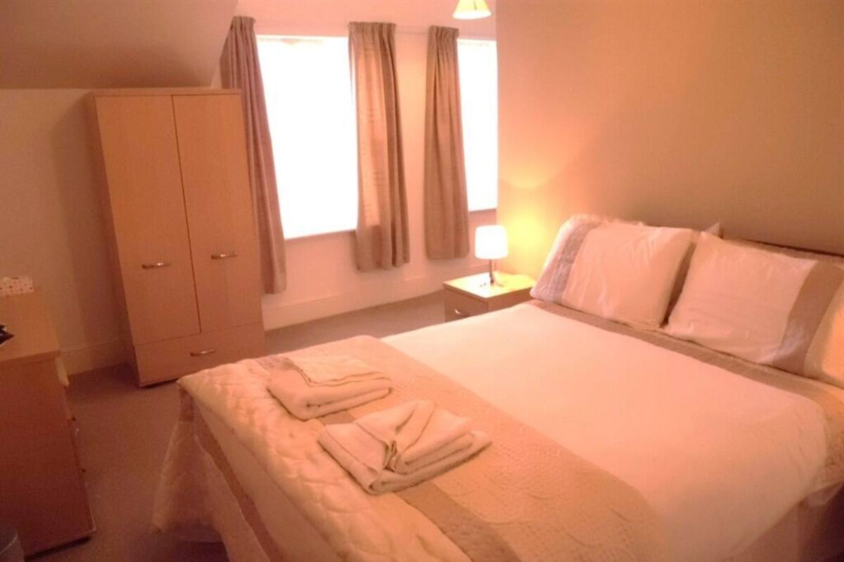 A hotel room with a bed, a wardrobe, a nightstand with a lamp, and curtains on the window.