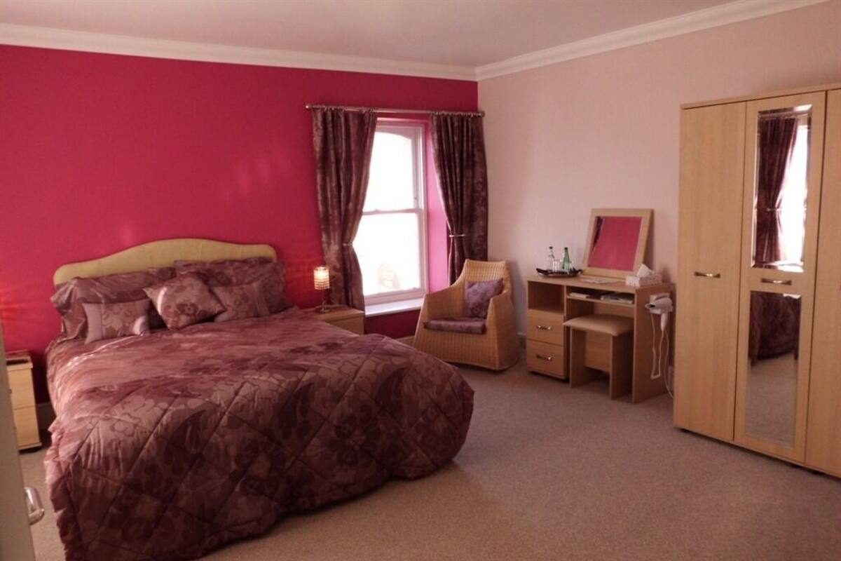 A bedroom with a large bed, a desk, a chair, and a wardrobe.