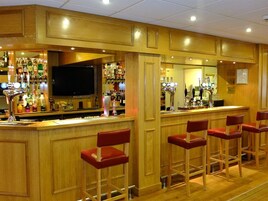 A bar area with wooden paneling, a television, and a variety of bottles and glasses on shelves.
