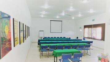 A conference room with rows of tables and chairs, a projector screen, and posters on the wall.