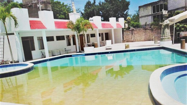 Una piscina con solárium empinado y cubierta, y un edificio de techo rojo al fondo.
