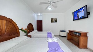 Una habitación de hotel con dos camas, televisión, ventilador de techo y un banco de madera.