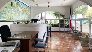 Un área de recepción con un gran mural, un mostrador de recepción, sillas y suelo de baldosas.