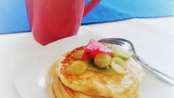 A stack of pancakes with fruit toppings on a white plate, a red mug, and a blue napkin.