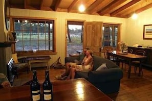 A cozy living room with a sofa, a coffee table with bottles, and a dining area with chairs and a table. - Lovedale Cottages (Lovedale)