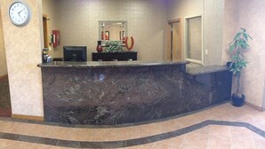 A reception area with a marble counter, a clock, a mirror, a vase, and a potted plant. - The Soluna Hotel (El Paso)