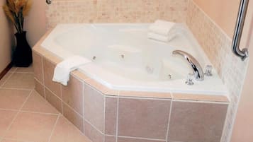 A corner bathroom with a freestanding bathtub, a towel, and a vase with dried flowers.