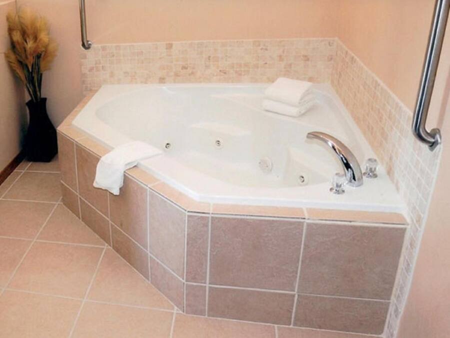 A corner bathroom with a freestanding bathtub, a towel, and a vase with dried flowers.