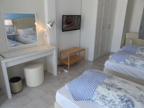 A hotel room with a desk, a bed, a small wooden table, a trash can, and a wardrobe. - Seafront Studios & Apartments (Chios)