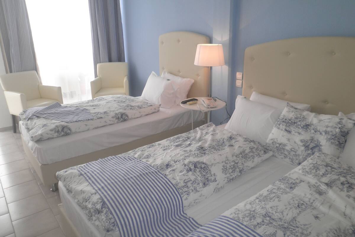 Hotellihuone, jossa on kaksi sänkyä. Jokaisessa sängyssä on kukallinen peitto, ja huoneessa on yöpöytä lampun kanssa sekä yksi tuoli.