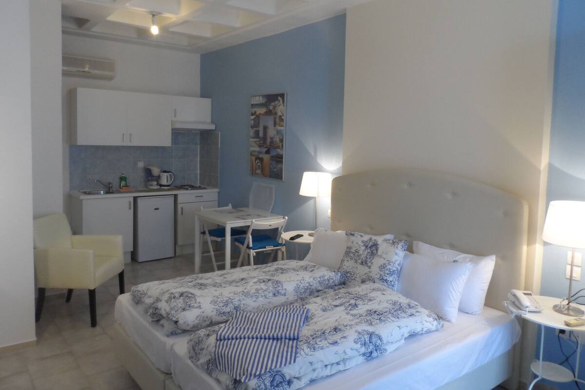 Hotellihuone, jossa on sänky, työpöytä, tuoli, pieni keittonurkkaus ja kylpyhuone.
