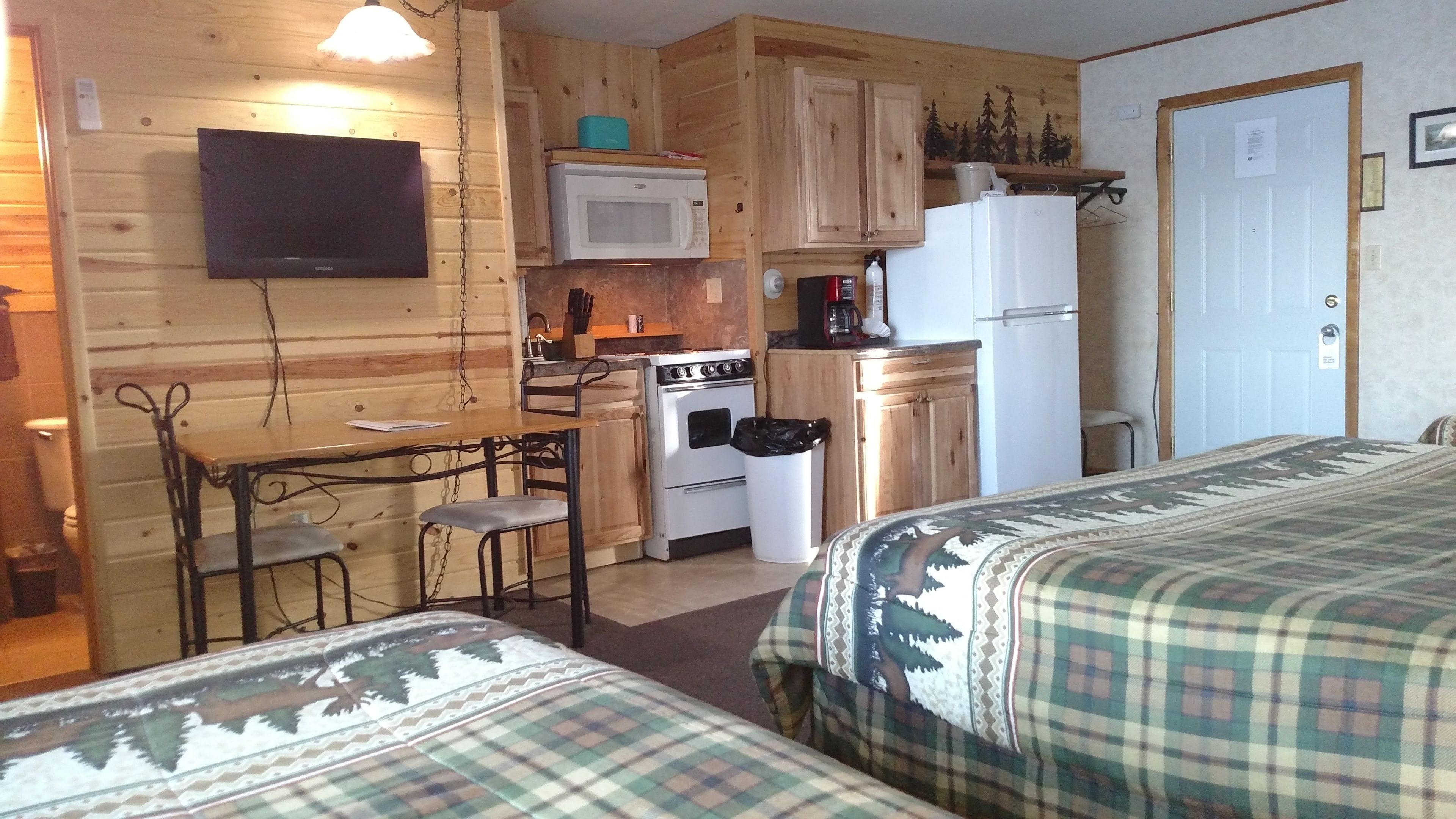 A compact room with a kitchenette, a dining table with chairs, and two beds with patterned bedding.