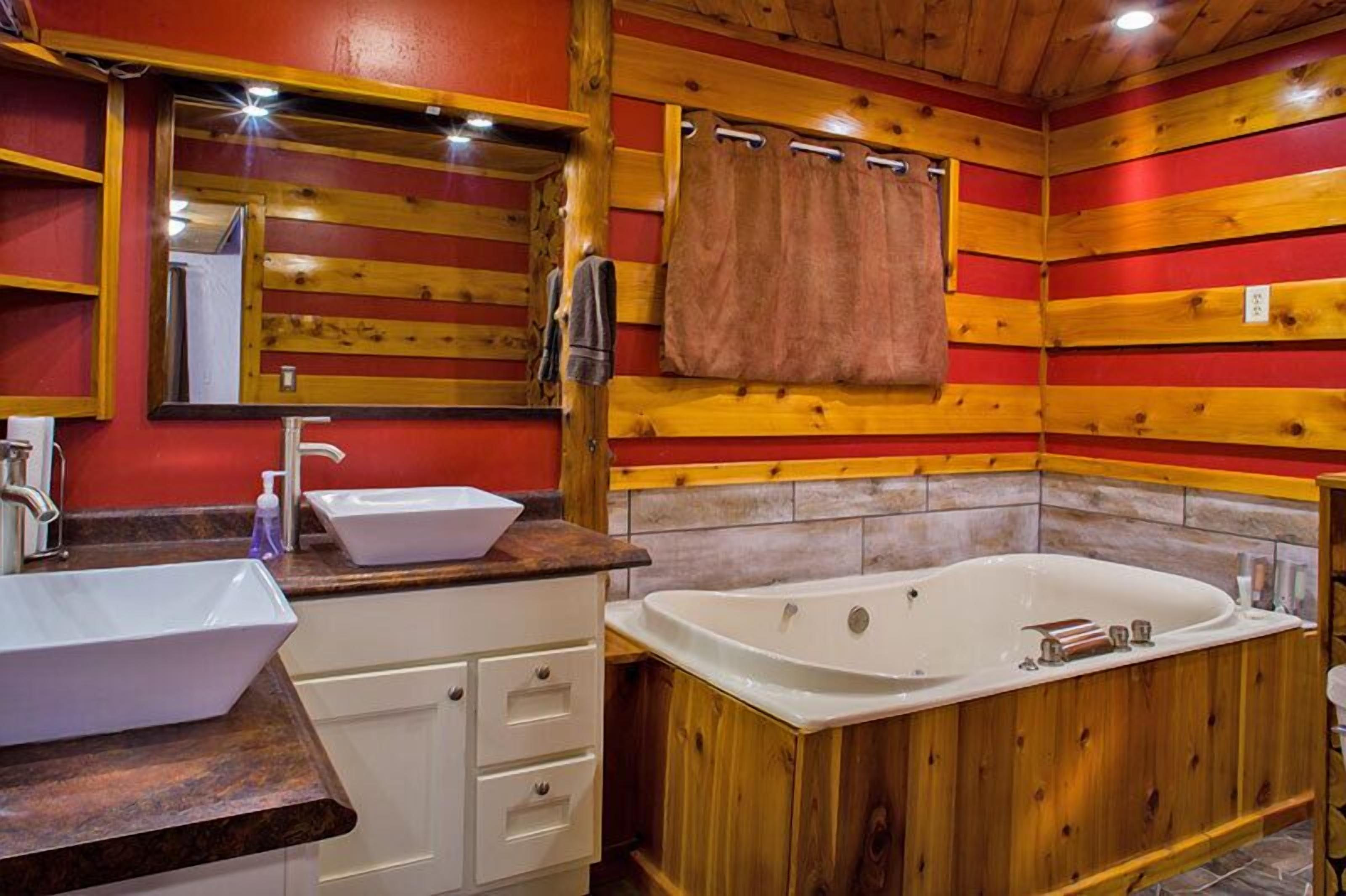 A wooden cabin-style bathroom with a large bathtub, a white sink, and a mirror.