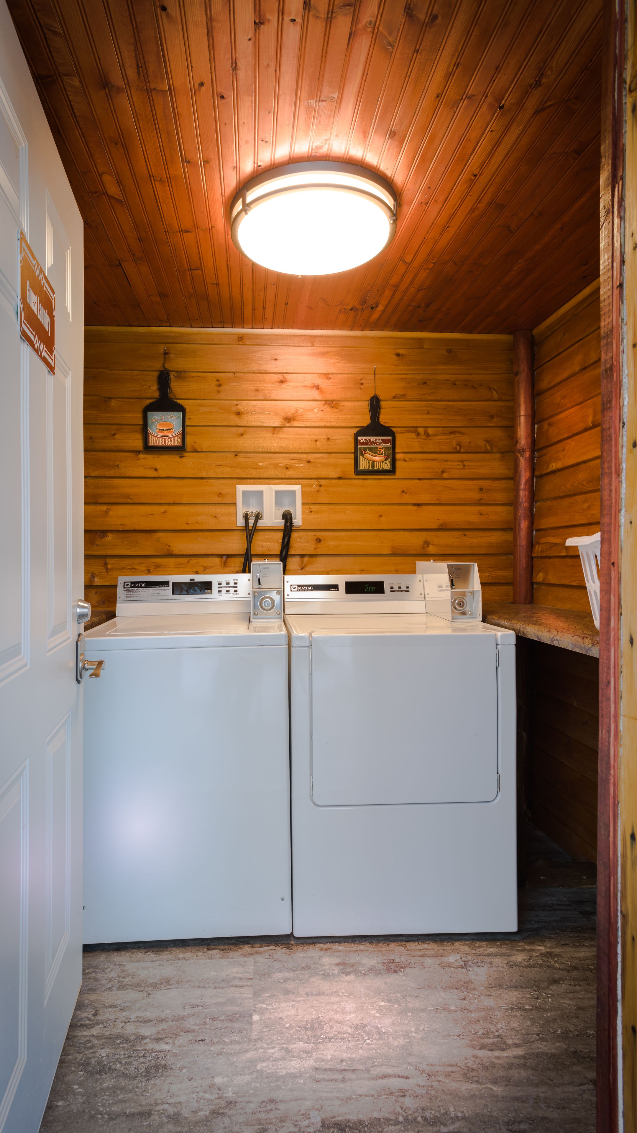 A laundry room with two white washing machines, wooden walls, and a ceiling light.