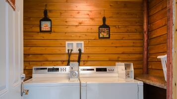 A laundry room with two white washing machines, wooden walls, and a ceiling light.