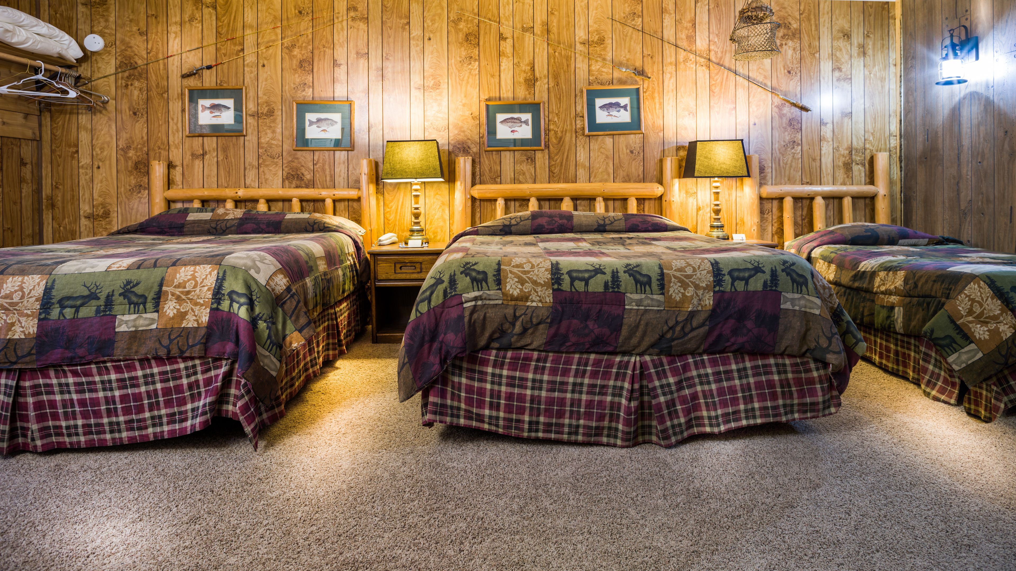 Una habitación con tres camas de madera, cada una con cubrecama acolchado estampado con motivos animales. Hay cuadros en la pared, una lámpara colgante y un banco de madera.