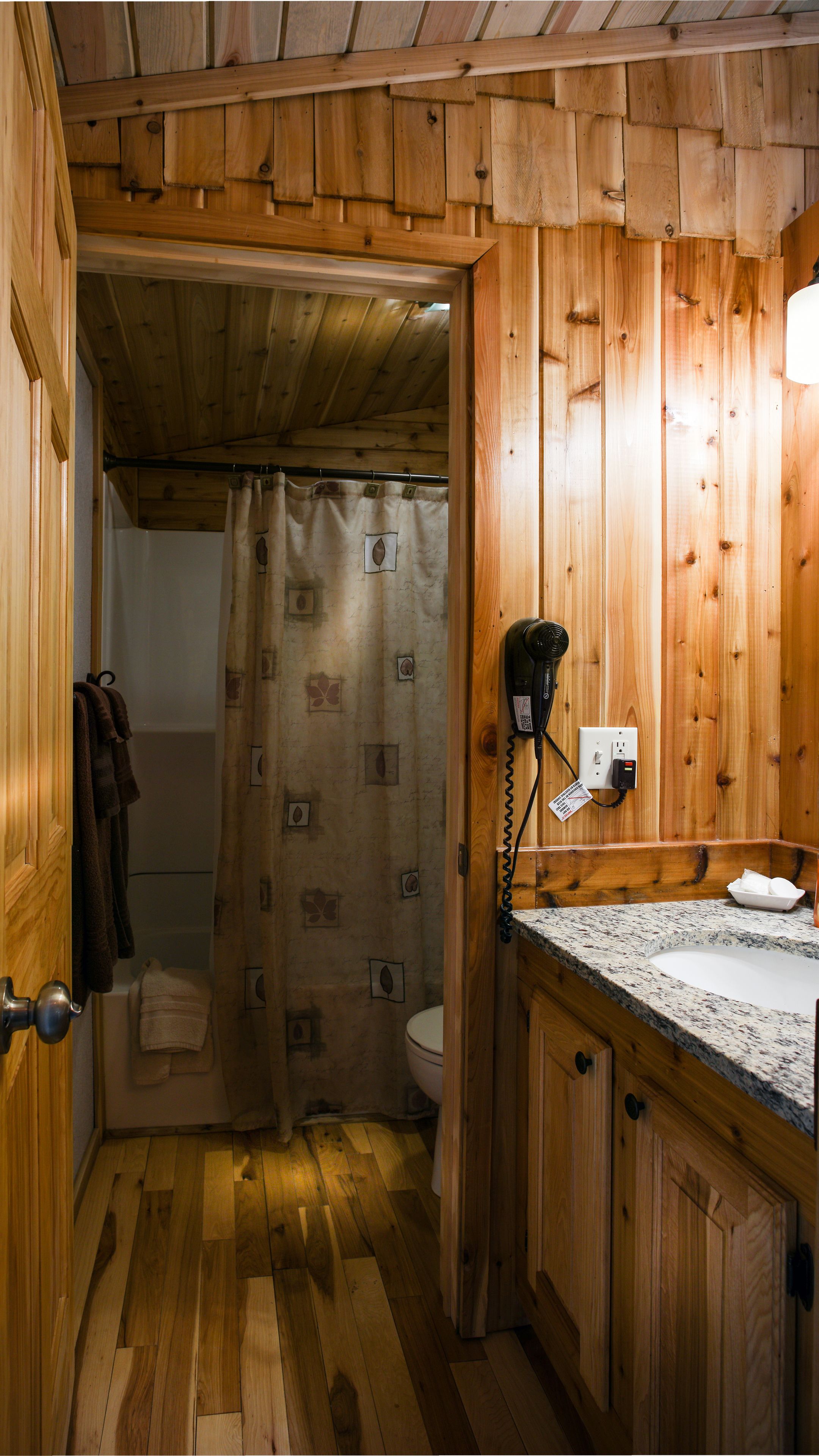 A wooden bathroom with a shower, a hairdryer, and a sink.