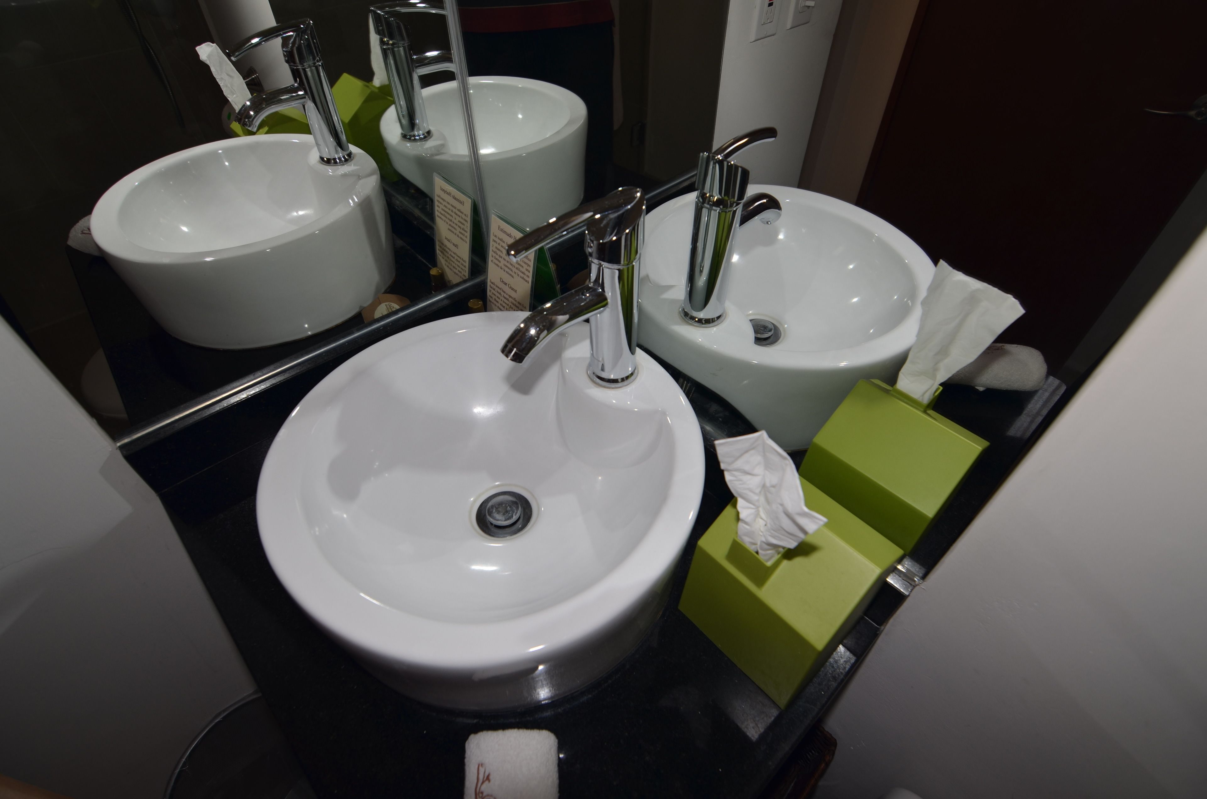 A bathroom with two sinks, a mirror, and a green soap dispenser.