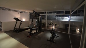 Een fitnessruimte met trainingsapparatuur, waaronder een loopband, krachtapparaat en hometrainer.