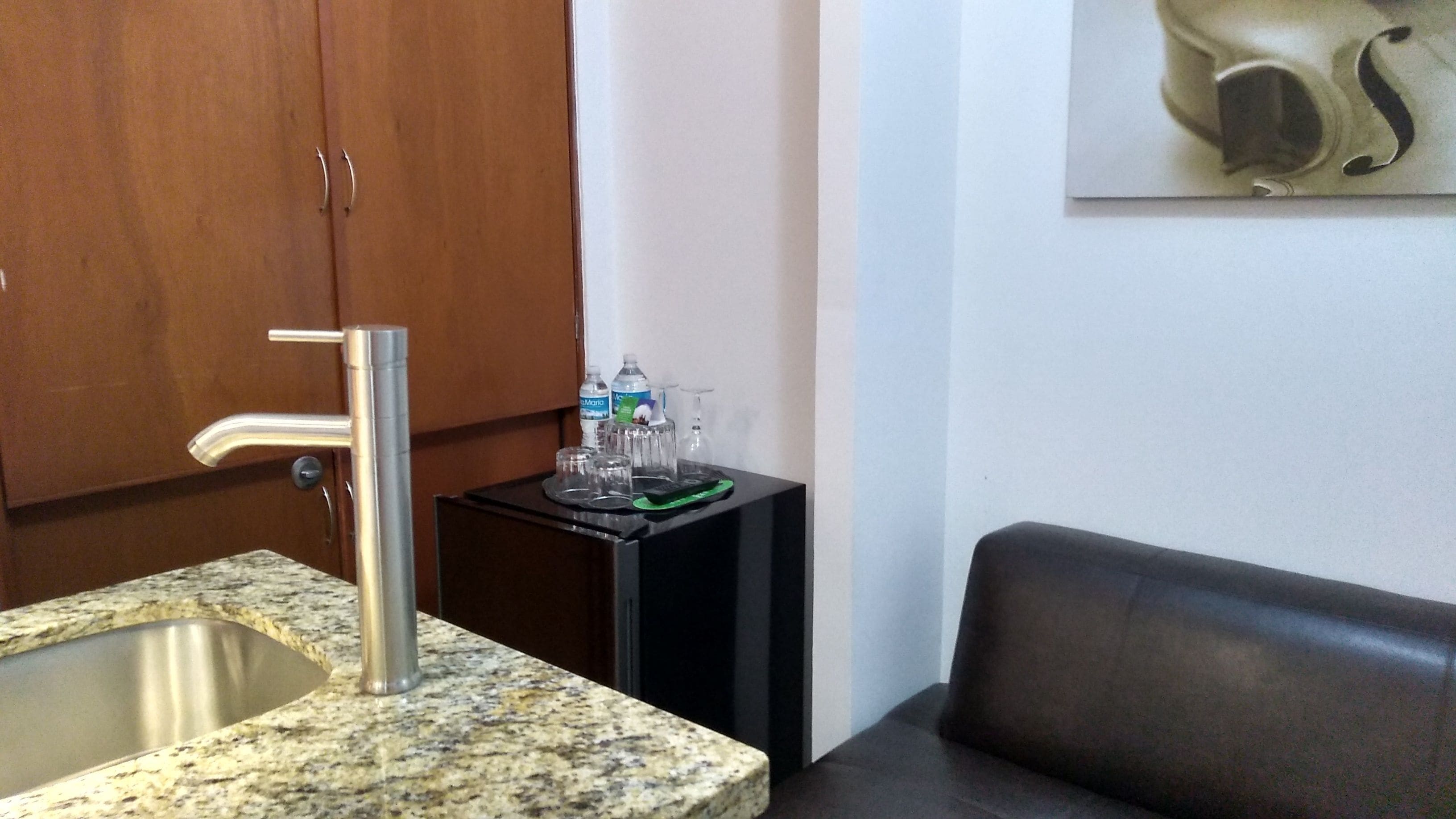 A kitchen with a granite countertop, stainless steel sink, and a small black table with water bottles and a remote control.