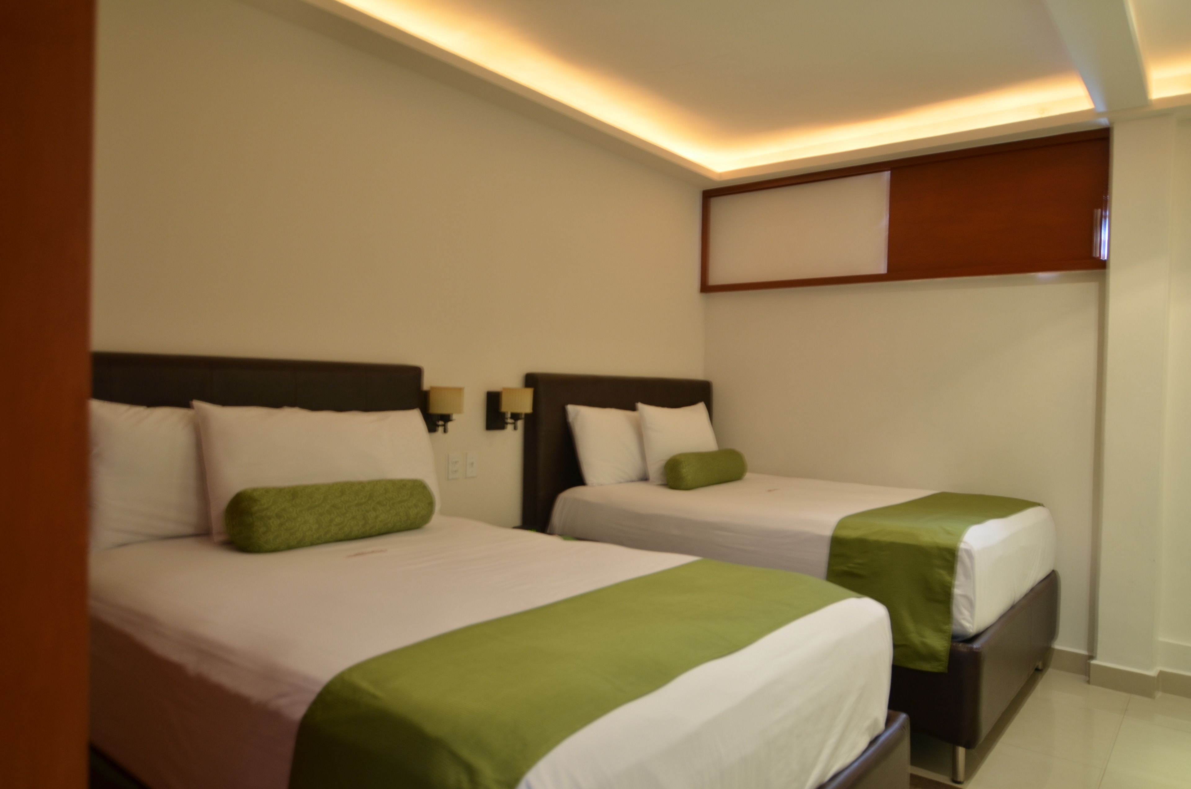 Une chambre d’hôtel avec deux lits, chacun recouvert d’une courtepointe verte et blanche, et une petite table de chevet.