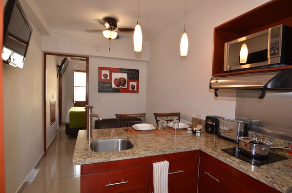 A kitchen with granite countertops, a sink, a microwave, a toaster, and a stove. There is a dining area with a table and chairs. - Suites La Concordia (Puebla)