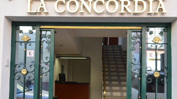 De ingang van La Concordia met decoratieve groene deuren en een trap die erheen leidt.