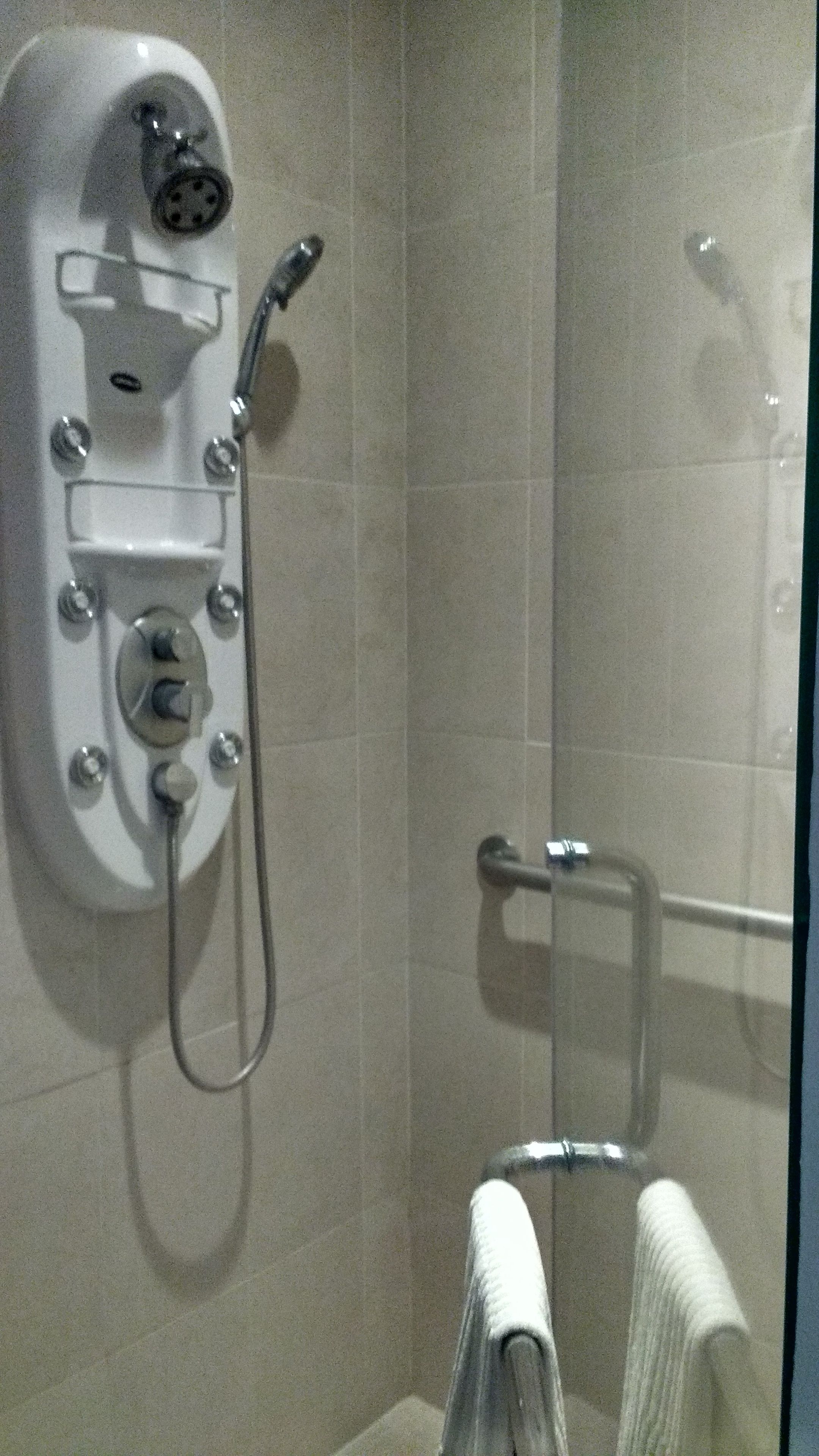 Una ducha con cabezal de ducha de mano, panel de control en la pared y toallero con una toalla.