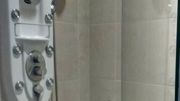 Una ducha con cabezal de ducha de mano, panel de control en la pared y toallero con una toalla.