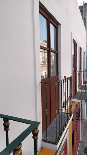 A building with a white facade, brown window frames, and a green and yellow balcony railing. - Suites La Concordia (Puebla)