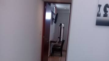 Un pasillo con un sofá de cuero negro, suelo de baldosas y una puerta que da a una habitación con un espejo y una silla.