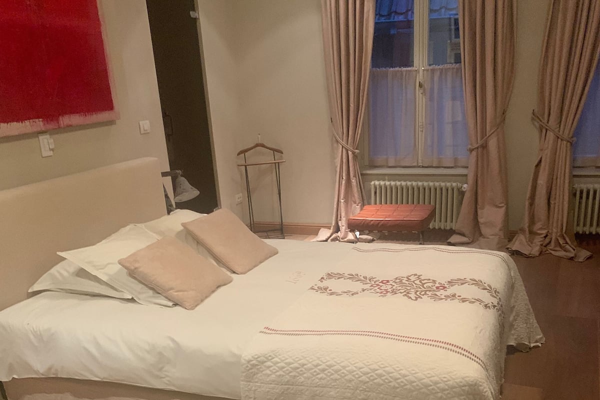 Un dormitorio con cama, radiador, ventana con cortinas y suelo de madera.