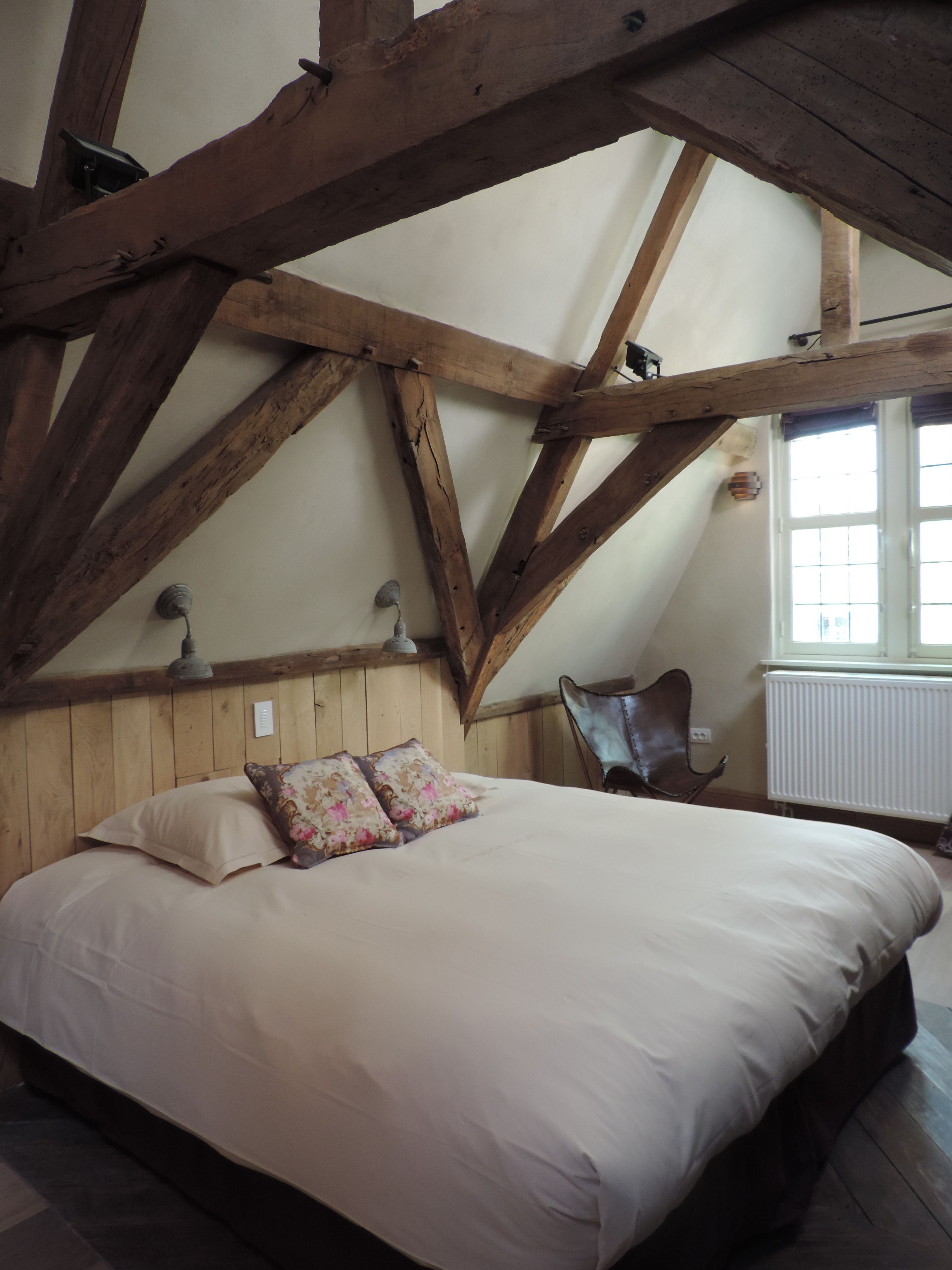 Een slaapkamer met een groot bed, houten balken, een radiator en een raam.