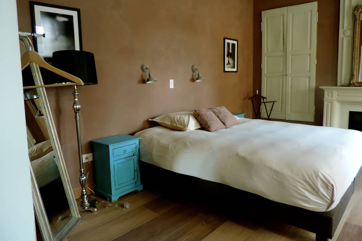 Un dormitorio con cama, mesitas de noche, cómoda, espejo y chimenea.