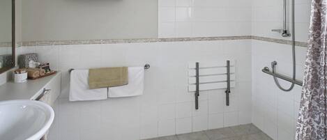 A bathroom with a sink, towel rack, shower, and a tiled floor.