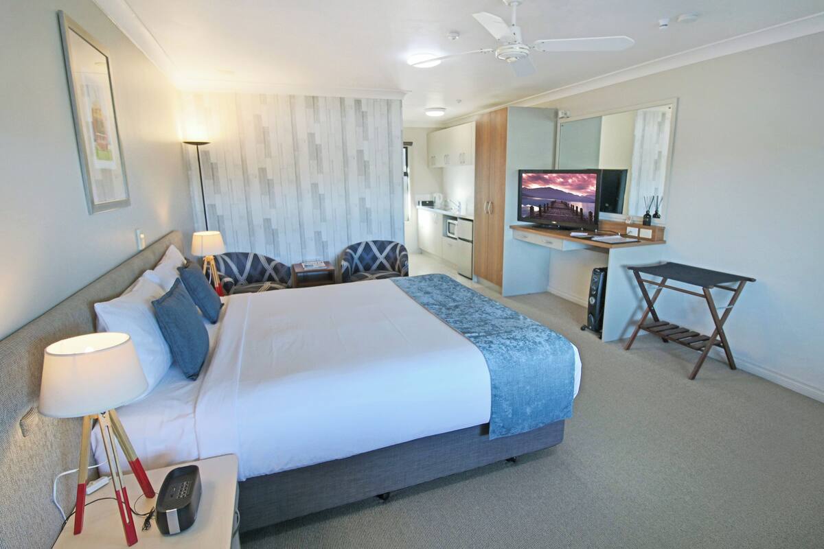 A modern hotel room with a large bed, a desk, a television, and a bathroom visible in the background.