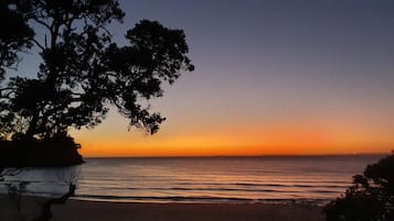Une plage où l’on peut admirer le coucher de soleil, avec une eau calme et des arbres qui encadrent le paysage.