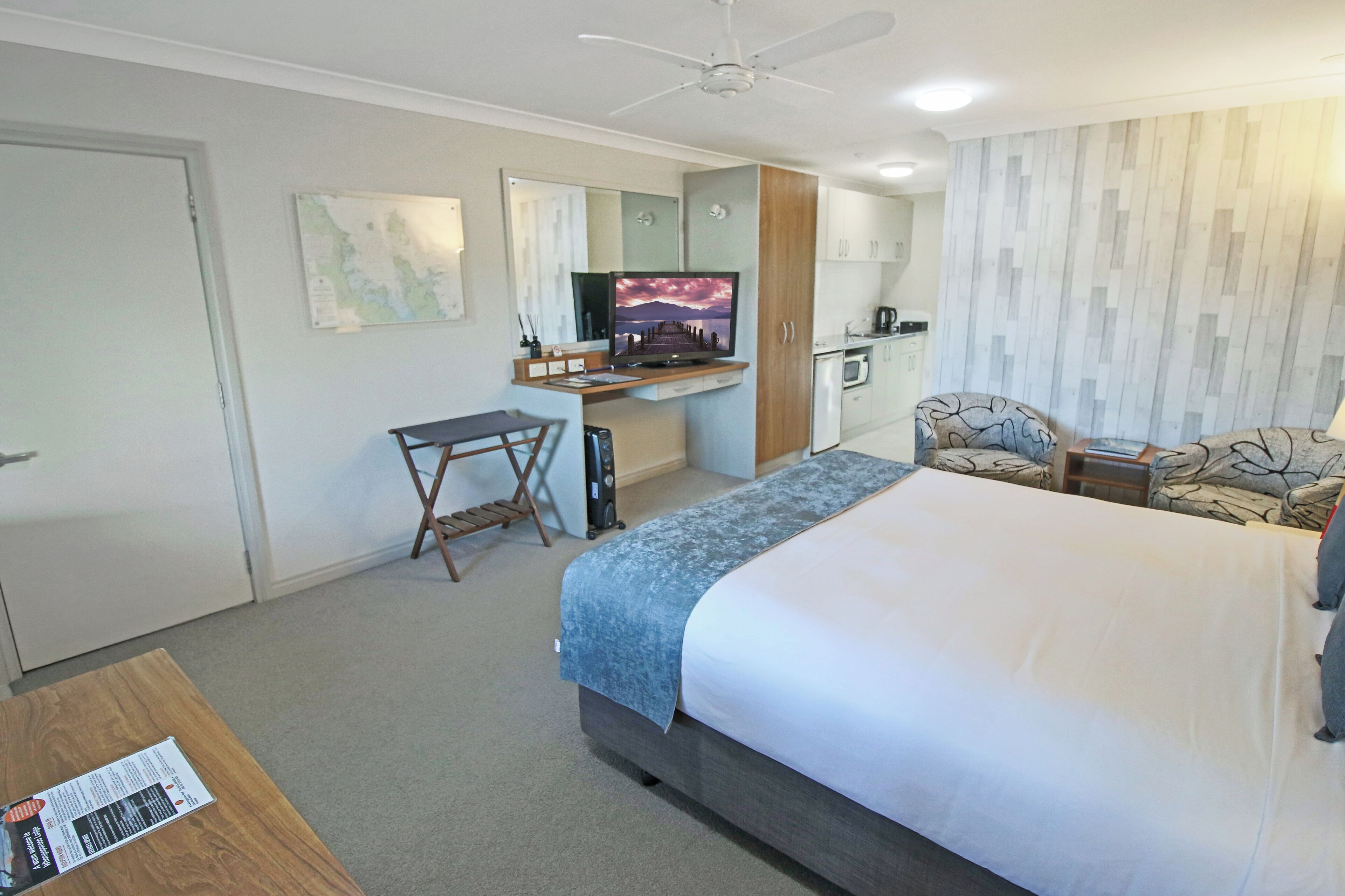 A hotel room with a bed, desk, chair, television, and kitchenette.