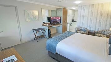 A hotel room with a bed, desk, chair, television, and kitchenette.