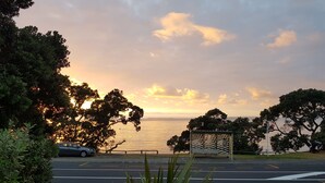 A road with a bench and a car parked on the side. - Whangaparaoa Lodge Motel (Whangaparaoa)